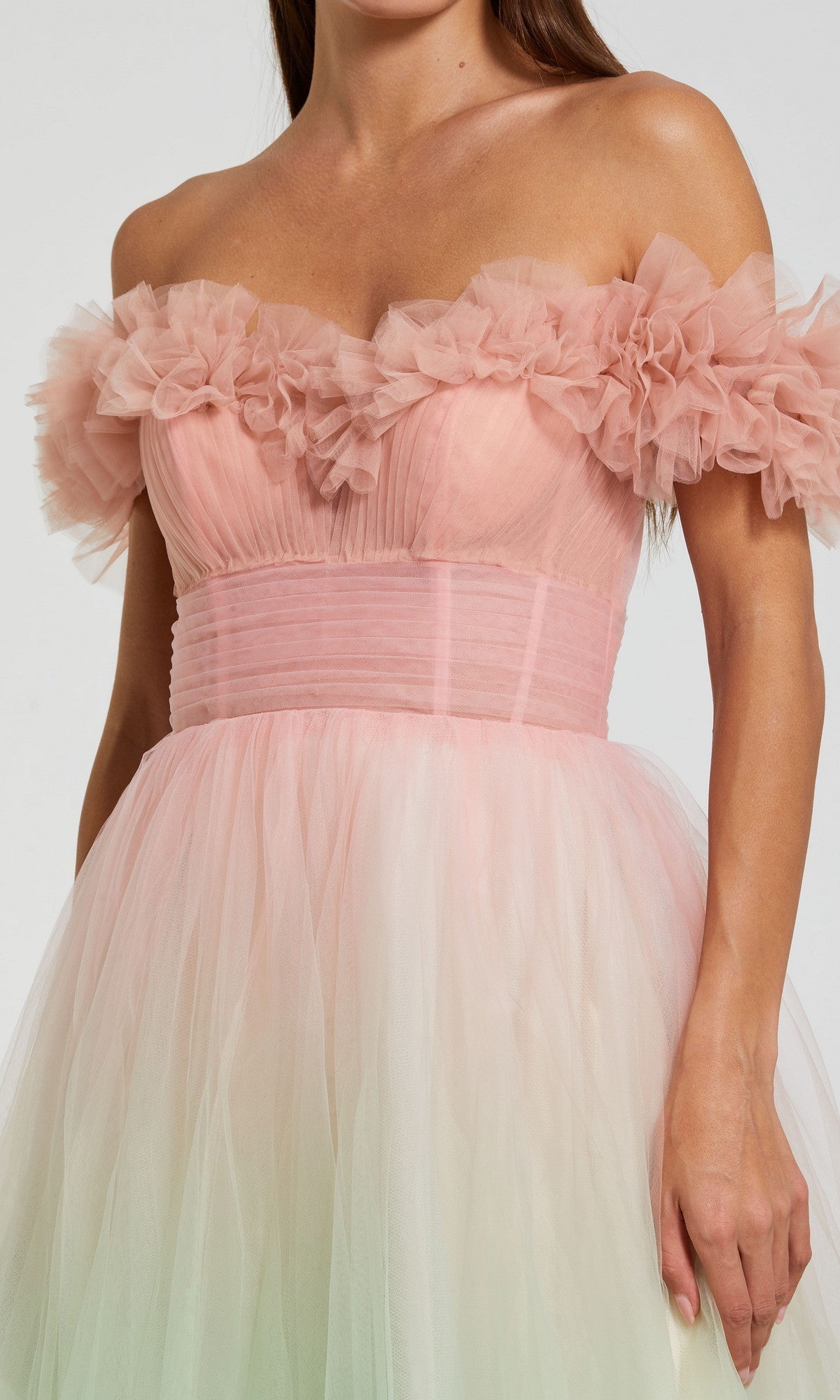 A woman wearing the Mac Duggal 37002 long prom dress—a pastel pink, off-shoulder tulle gown with ruffled bodice detailing and a fitted waist, exuding dreamy ombre elegance.